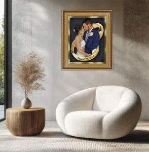 Two Rings, One Heart Painting, Bride brunette in white lace gown, groom dark haired in navy suit facing each other within a set of gold wedding bands, displayed framed on a living room wall. 